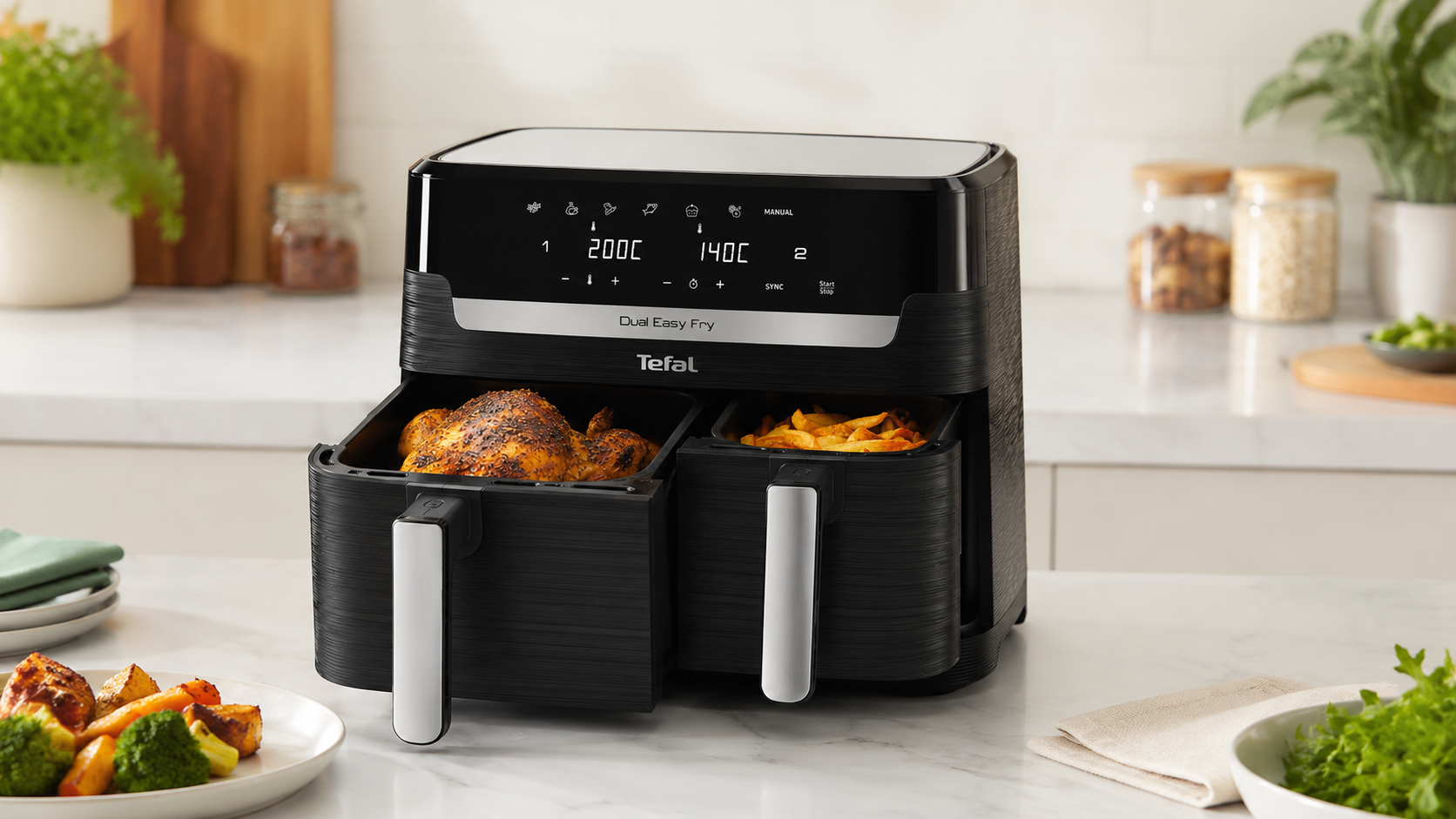 Black Tefal Easy Fry Dual Zone air fryer with two open drawers — a whole roast chicken in the larger drawer and chips in the smaller drawer — on a bright kitchen worktop.